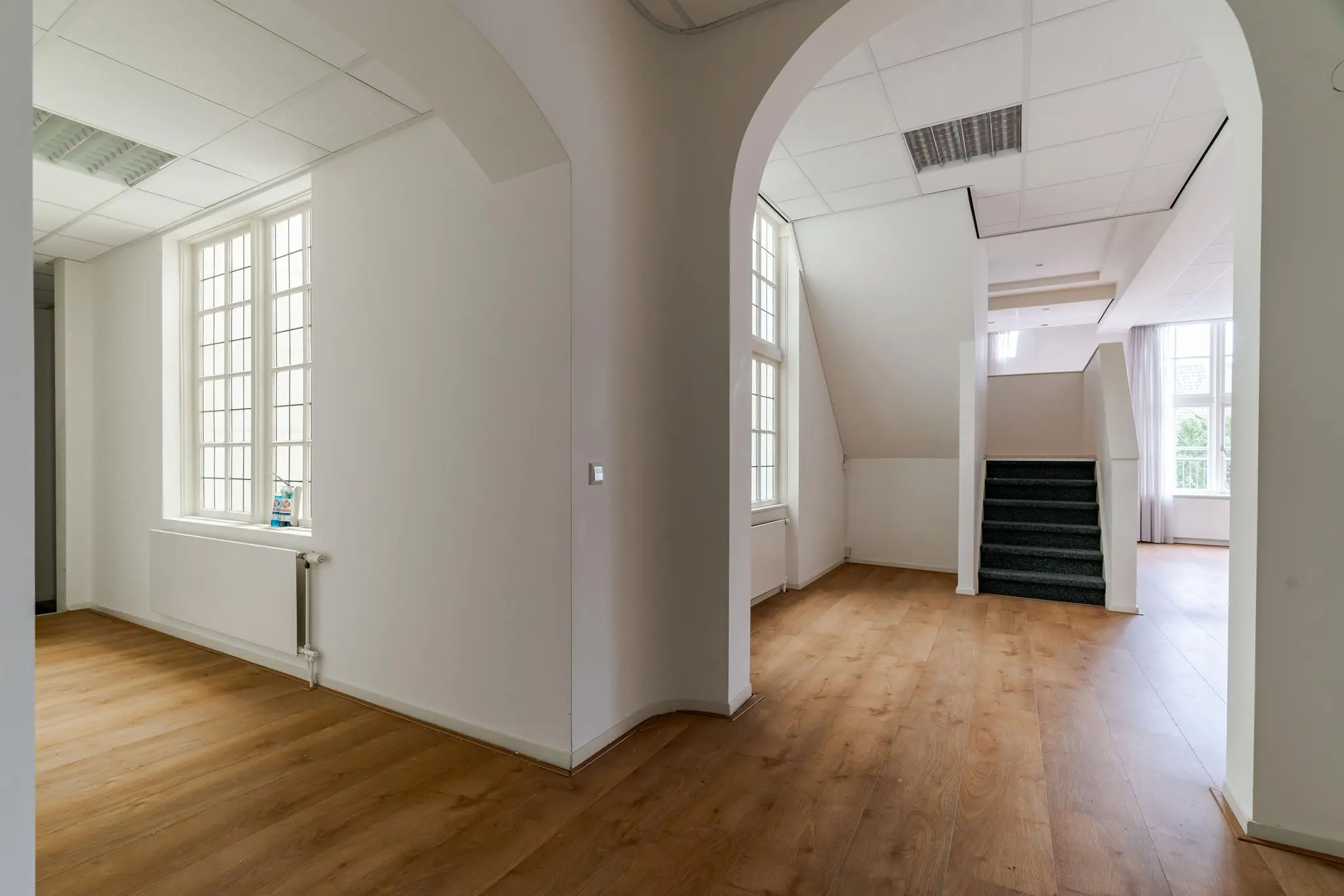 Lichte binnenruimte met houten vloer, grote ramen en een trap naar boven in een pand aan het Lange Voorhout.